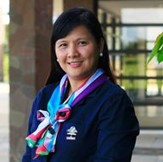 Carla has long black hair and is wearing a blue sweater with a colorful scarf